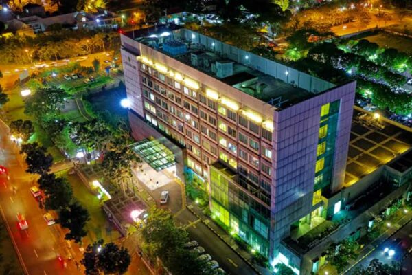 Vue aérienne de nuit d'une clinique privée de plusieurs étages, façade éclairée et avenue passante