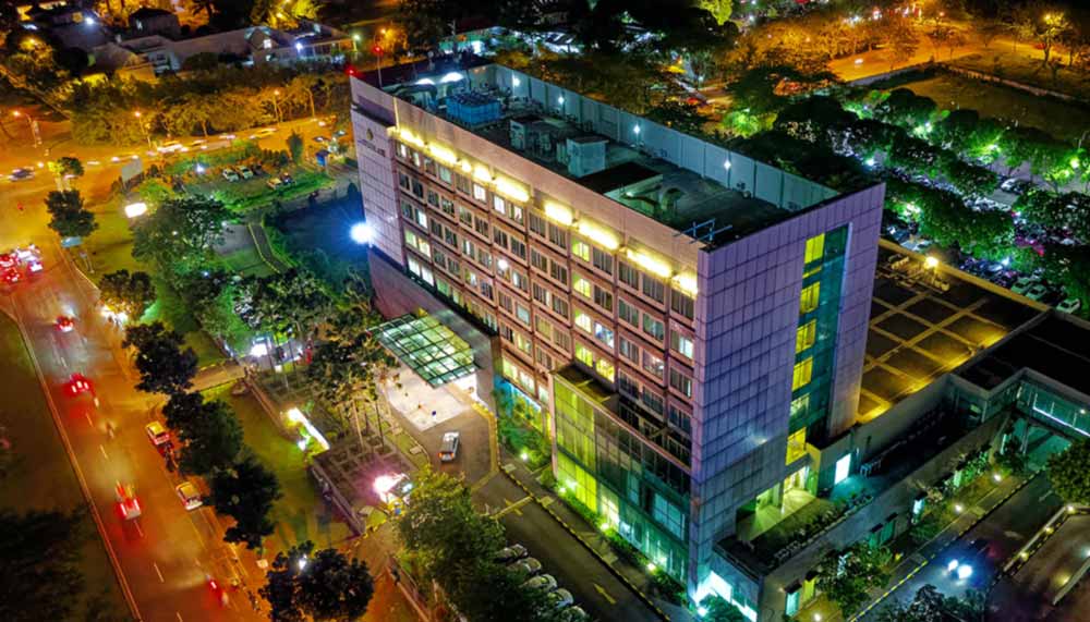 Vue aérienne de nuit d'une clinique privée de plusieurs étages, façade éclairée et avenue passante