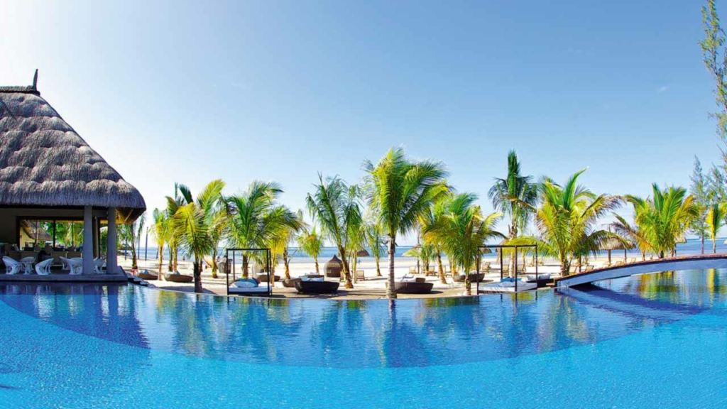 Piscine d'hôtel et paillote au bord d'une plage de l'île Maurice, palmiers couchés par le vent