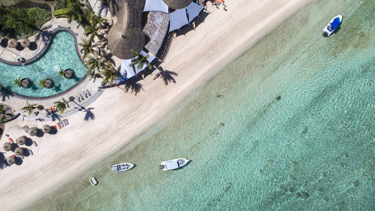 Vue aérienne verticale d'une plage d'hôtel de l'île Maurice, avec piscine, parasols et bateaux au mouillage