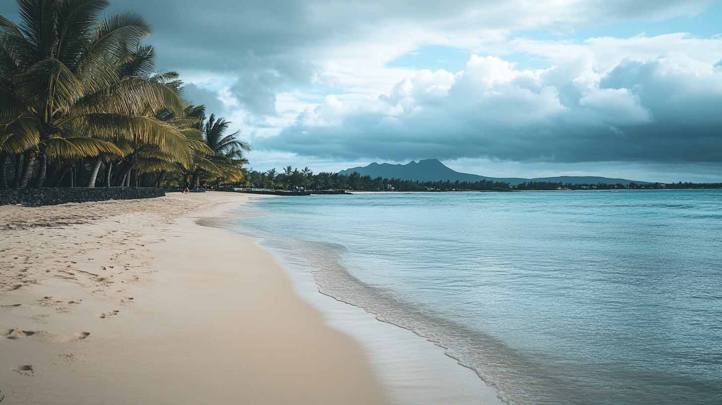 Plage de l'île Maurice bordée de cocotiers sous un ciel chargé de nuages, montagne à l'horizon