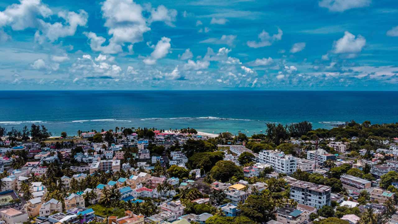 Vue aérienne d'une ville côtière de l'île Maurice : quartiers résidentiels, lagon et barrière de corail au large.